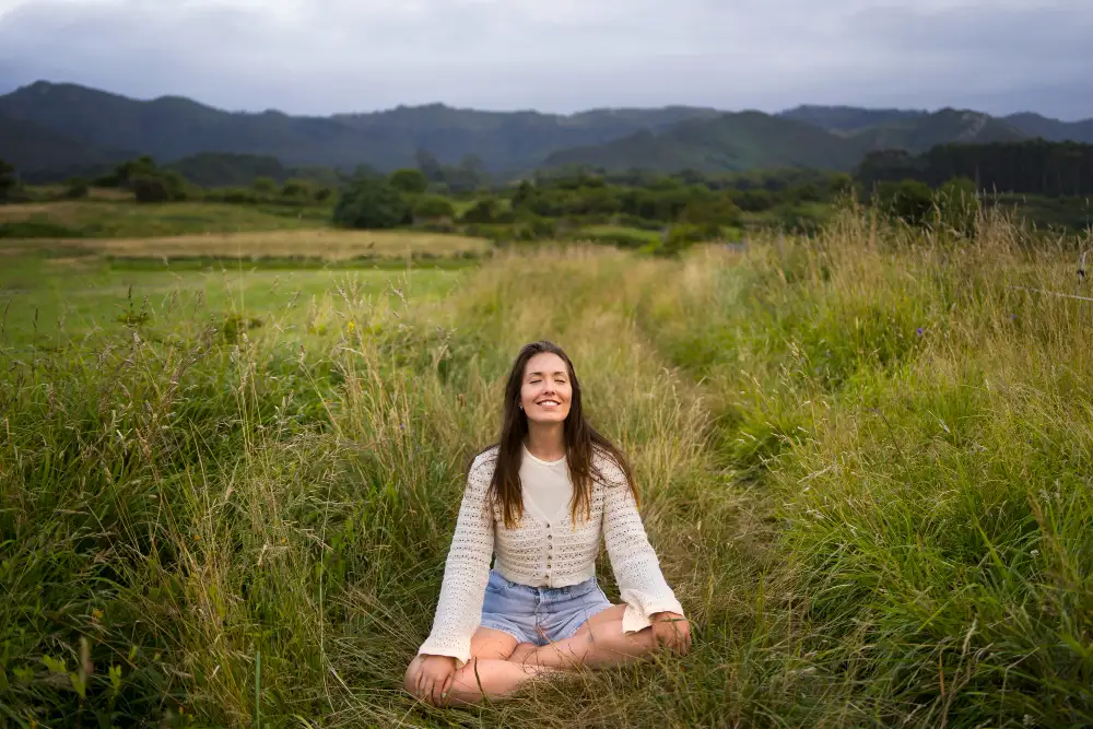 Mujer sentada en posición de loto en un campo, disfrutando de la tranquilidad y el aire libre, ideal para ilustrar el bienestar físico y emocional que promueve el turismo transformador.