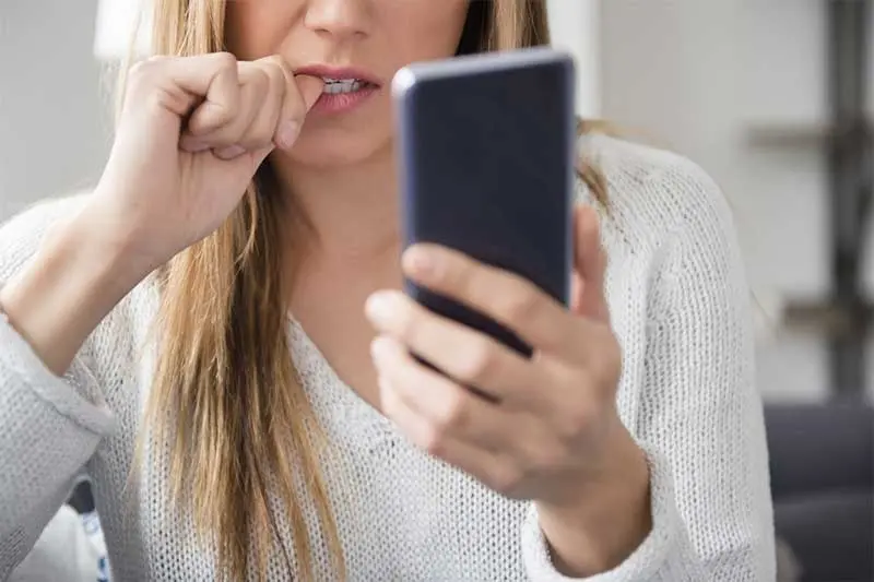 Joven mordiéndose el dedo por usar el celular