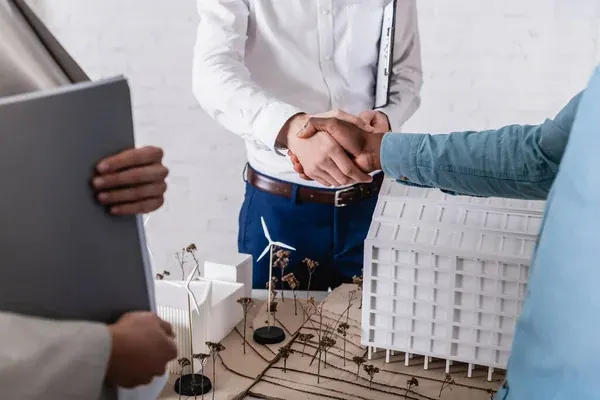 hombre de negocios estrechando la mano con su socio de negocios cerca de la maqueta de la central eléctrica alternativa