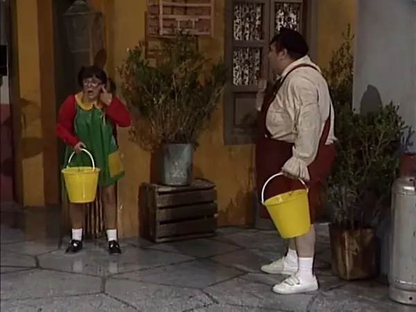 Personajes intentando bañar al Chavo con cubetas de agua en la vecindad.
